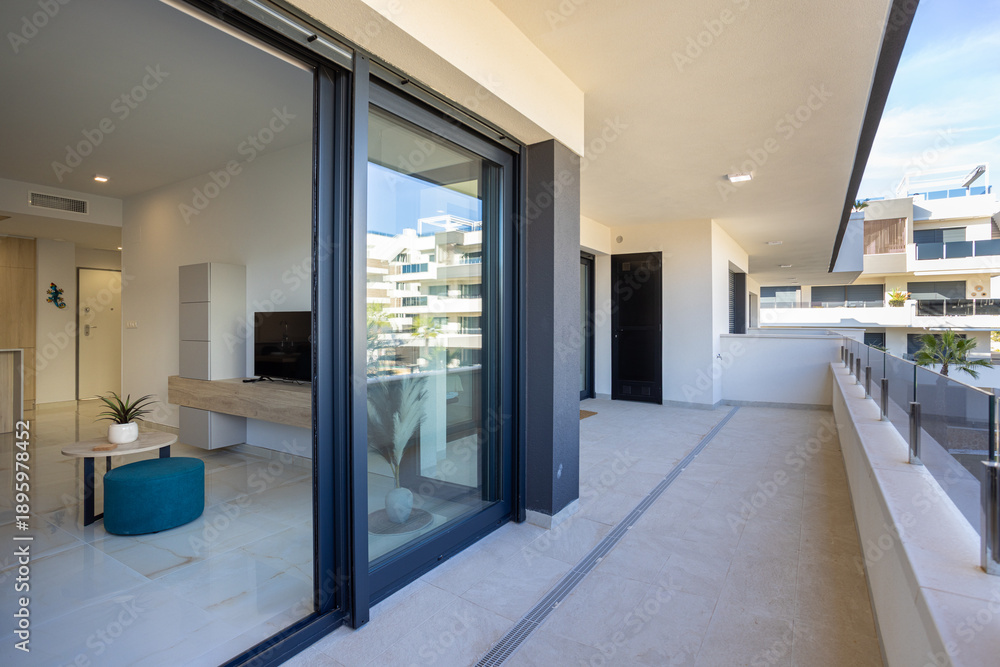 Naklejka premium Modern apartment balcony with glass railing and interior view through large sliding doors