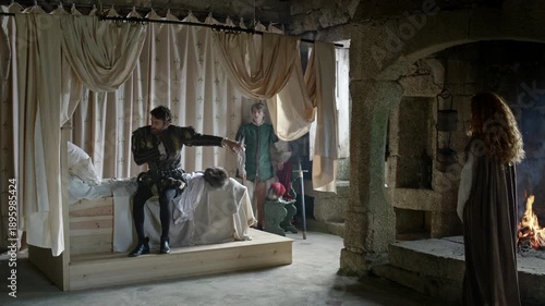 Inside a castle room, two people engage in conversation while another person stands nearby. A fire burns in the fireplace, creating warmth in the stone setting.