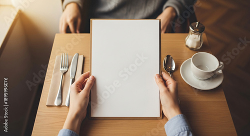 Close-up of hands holding a blank white menu or document mockup at a warm, inviting restaurant table, perfect for custom design and presentation