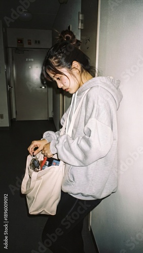 Young Asian woman searching for keys in tote bag in apartment hallway