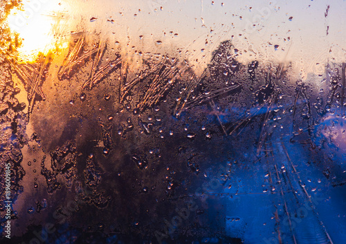 Cuadro en lienzo Window pane showing intricate ice patterns and water droplets reflecting a warm