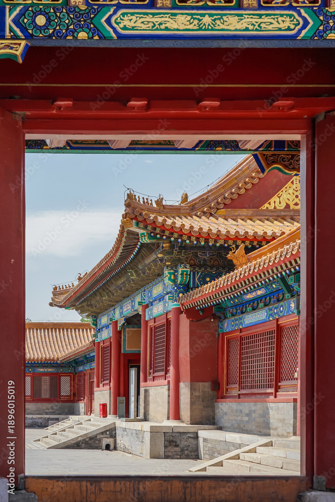Fototapeta premium The Forbidden City,Traditional Chinese palace architecture viewed through a red wooden doorway with ornate roof details and vibrant colors.