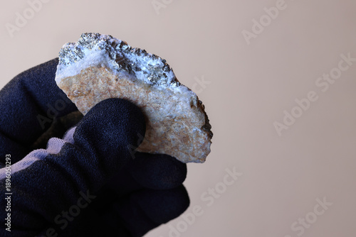Valokuva Hand with safety glove holding a piece of quartz gold (Au) ore against tan background