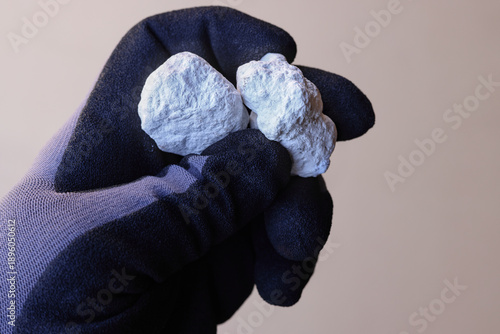 Photography Hand with safety glove holding Magnesite ore against tan background