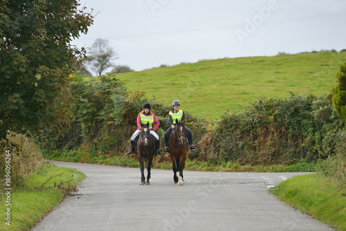 Two people riding their horses on a quiet country road in rural Shropshire, enjoying being together in nature.The riders are wearing safety gear so that other road users will see them.