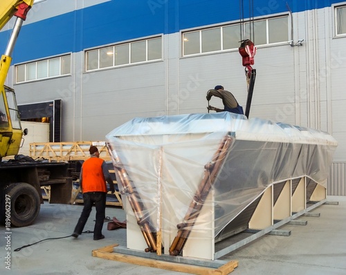 Workers prepare a large industrial chiller for transport outside of a manufacturing facility.
