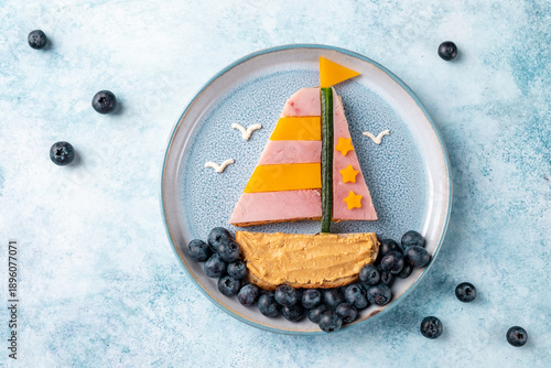 Creative food art with a sailboat made from fruits, placed on a plate with blueberries and a simple background