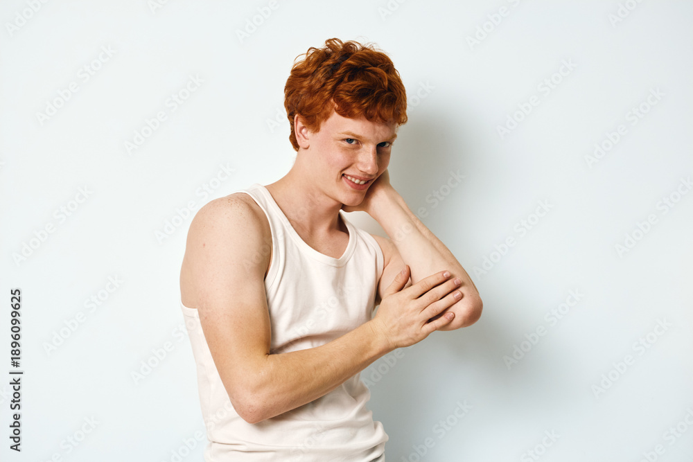 Φωτογραφία Young man with red hair wearing white tank top posing and smiling against white background indoor, casual style and confident expression for portrait photo