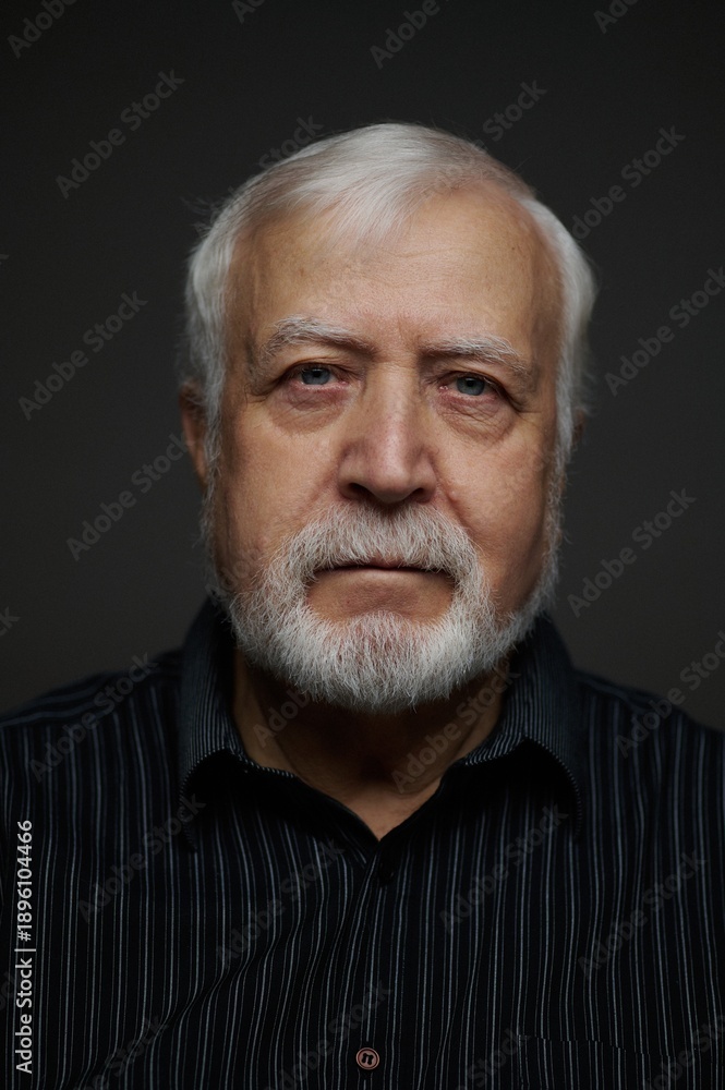Fototapeta premium Elderly man poses for a close-up photo in a dark setting with focused lighting showing his features and expression clearly