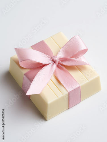 A luxurious and minimal gift box made entirely of creamy white chocolate, elegantly tied with a soft pink satin ribbon and bow, isolated on a white background.