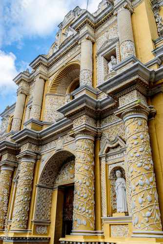 Iconic yellow facade of Convento de La Merced in Antigua Guatemala showcasing stunning Spanish Baroque architecture against a vibrant sky