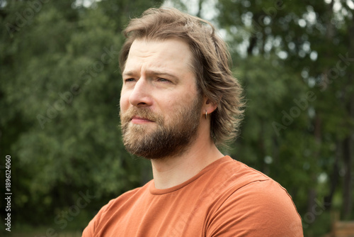 Portrait of handsome young man in orange t-shirt outdoors. Male with long hair and beard feel happy