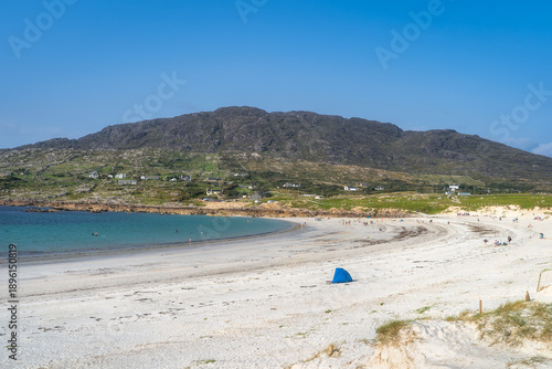 Blue beach umbrella on white sand near mountains at Dogs Bay in Connemara, Galway, Ireland. Lone shelter, beachcomber rest. Calm turquoise bay with soft breeze, minimal footprints and wide open sky