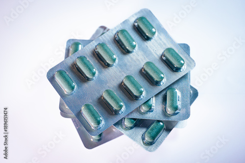 Green capsules in blister packs stacked on a white background, showcasing pharmaceutical packaging with multiple rows of pills clearly visible