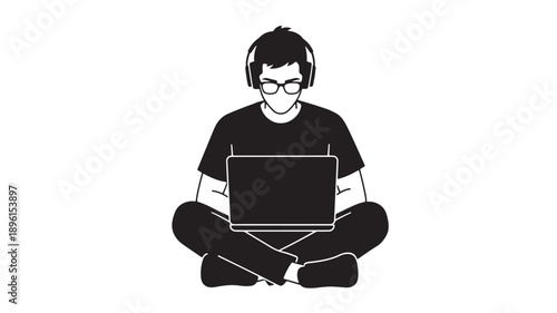 A man sitting cross-legged on the floor with a laptop on his lap and wearing headphones in a relaxed pose