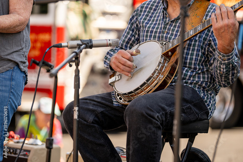 Photos Close-up of banjo player's hands plucking strings at outdoor performance with microphone nearby amplifying music