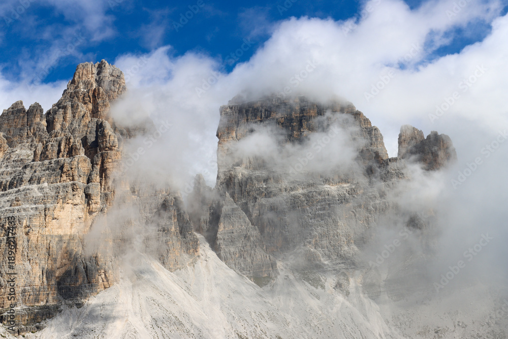 Fototapeta premium Clouds embrace the Tre Cime di Lavaredo from a mountain path