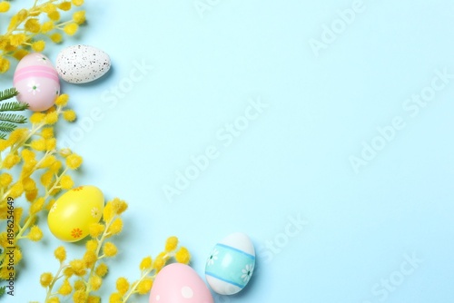 Easter concept. Top view photo of colorful easter eggs and bouquet of mimosa flowers on isolated blue background with copyspace