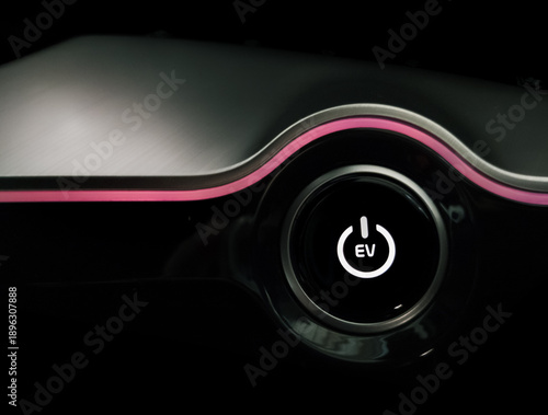 Close up of a glowing white electric vehicle power button with EV text on a sleek black dashboard featuring a pink ambient light strip in a modern car interior