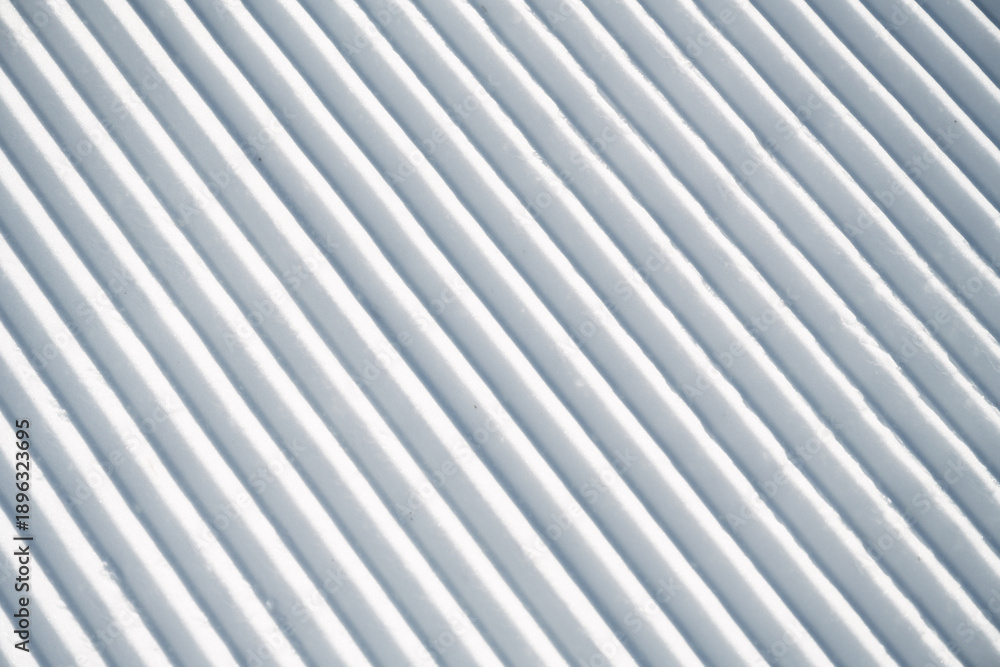 Obraz premium Corduroy snow texture on a freshly groomed ski slope, showing clean parallel ridges and detailed winter snow structure, ideal as background or texture for winter sports themes.