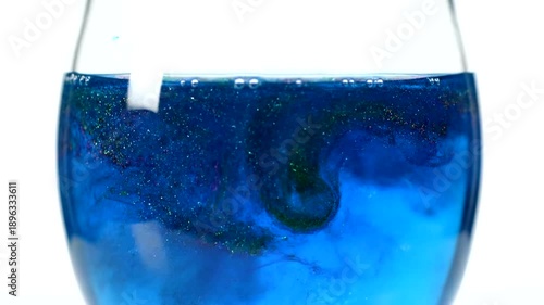 Close up of blue liquid swirling inside a clear glass.