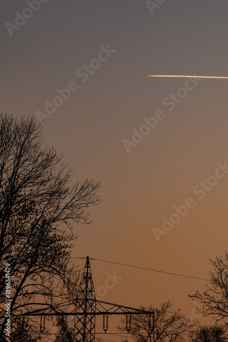 A jet leaves contrails in the sky at sunset.
