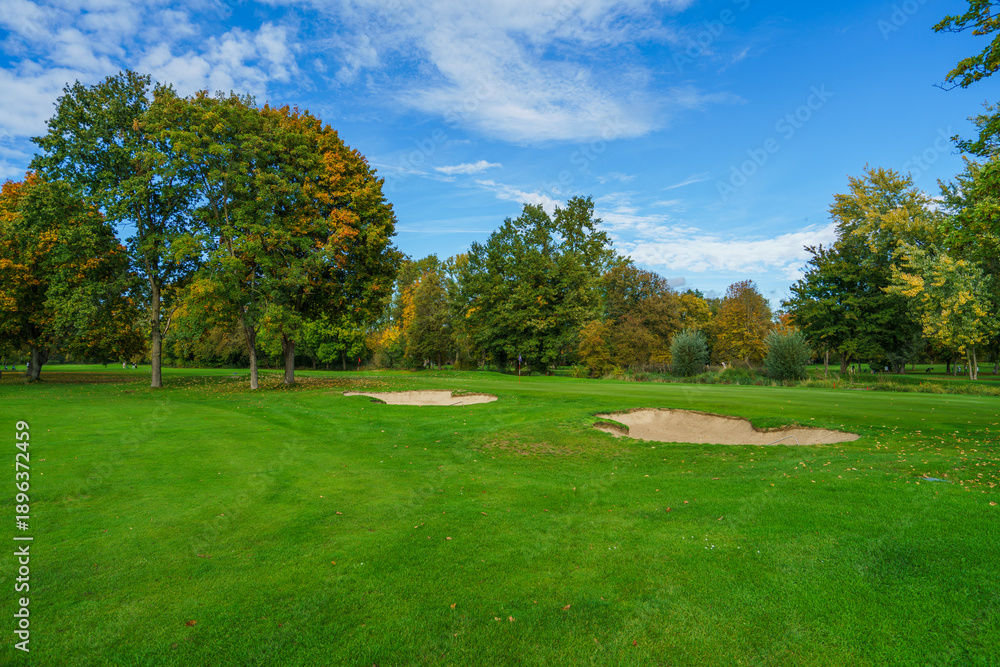 Obraz premium a professional golf course fairway featuring well-maintained sand traps and lush green grass. Beautiful autumn foliage on surrounding trees creates a peaceful outdoor sports atmosphere