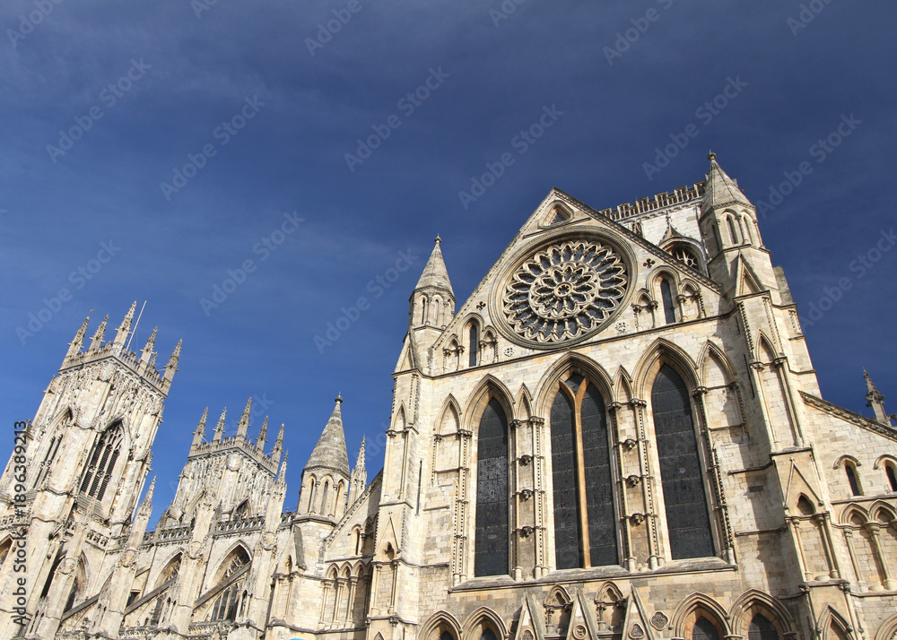 Fototapeta premium York Minster cathedral in York, England, showcasing Gothic architecture, towering spires, and an ornate rose window beneath a deep blue sky.