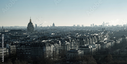 Panoramic view of Paris skyline featuring the golden dome of Les Invalides. Classic haussmann architecture and urban rooftops under a hazy winter sky in France