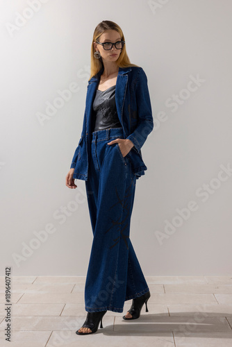 Woman in oversized denim suit and leather top posing in studio