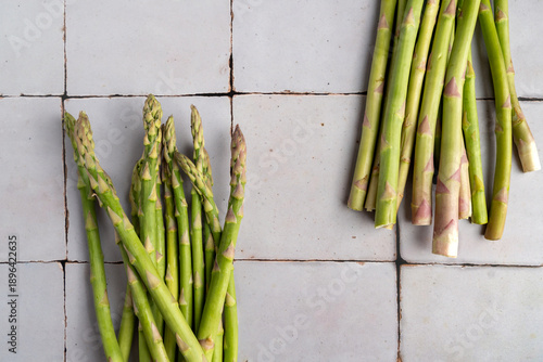 Raw green asparagus displayed on a neutral stone surface. Simple and rustic food composition highlighting fresh vegetables, organic food and natural cooking ingredients.