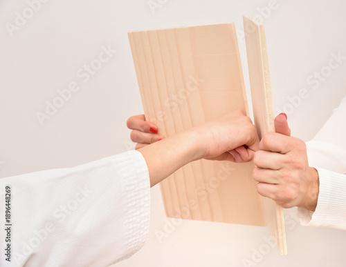 Young girl breaking a wooden board with her fist while practicing martial arts. Close-up. Youth, sport and healthy lifestyle concept. 