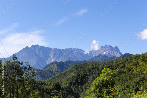 A high-angle view of Mount Kinabalu’s rocky peaks towering over a dense tropical forest canopy under a clear blue sky in Sabah, Malaysia.