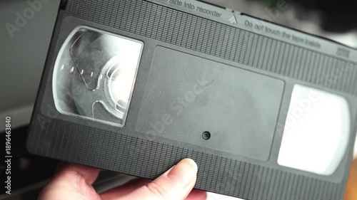 Close up of a hand holding a videotape. Retro vhs cassete in a player.	