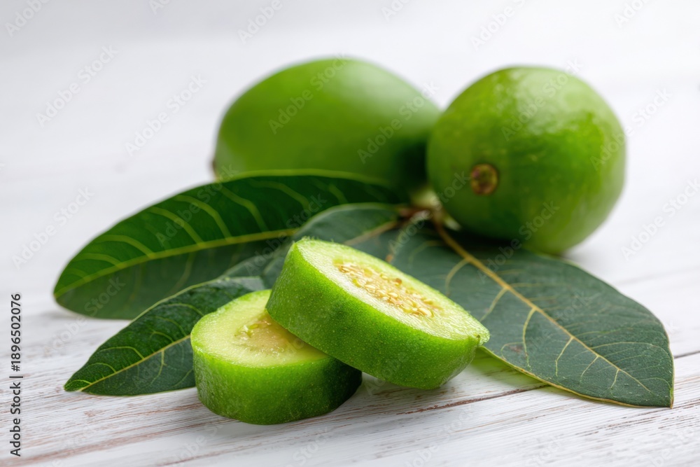 Obraz premium Fresh green guava slices and whole guavas with leaves on wooden surface