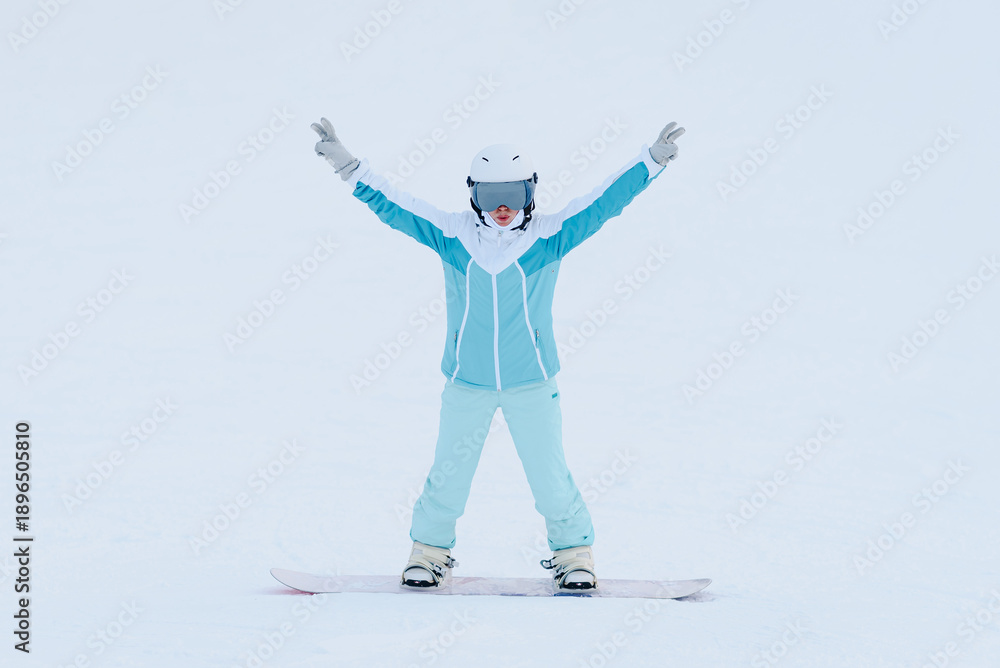 Fototapeta premium young active caucasian woman snowboarding, white and blue sports clothes, white helmet, purple snowboard, sportive woman stands on snowboard, cloudy winter day, mountain slope, equipped ski run