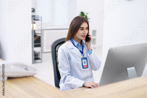 Slika na platnu Medical assistant answering phone while working on computer at reception in clin