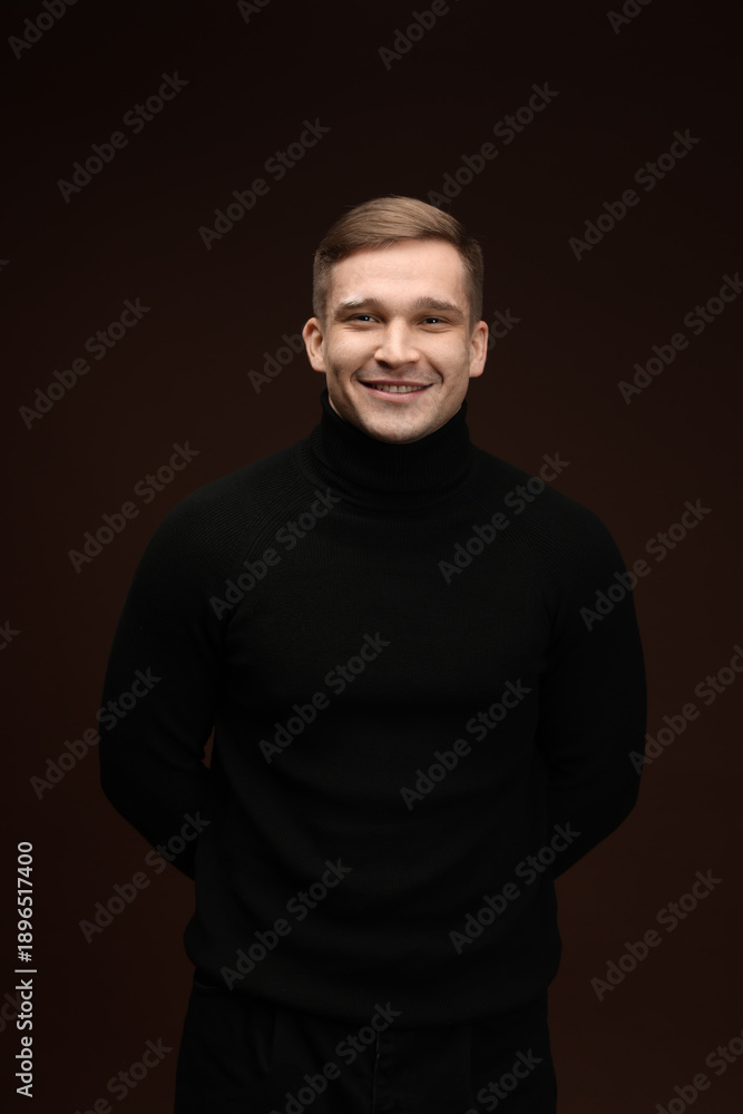 Fototapeta premium Fashion model. Portrait of smiling man posing against dark brown background
