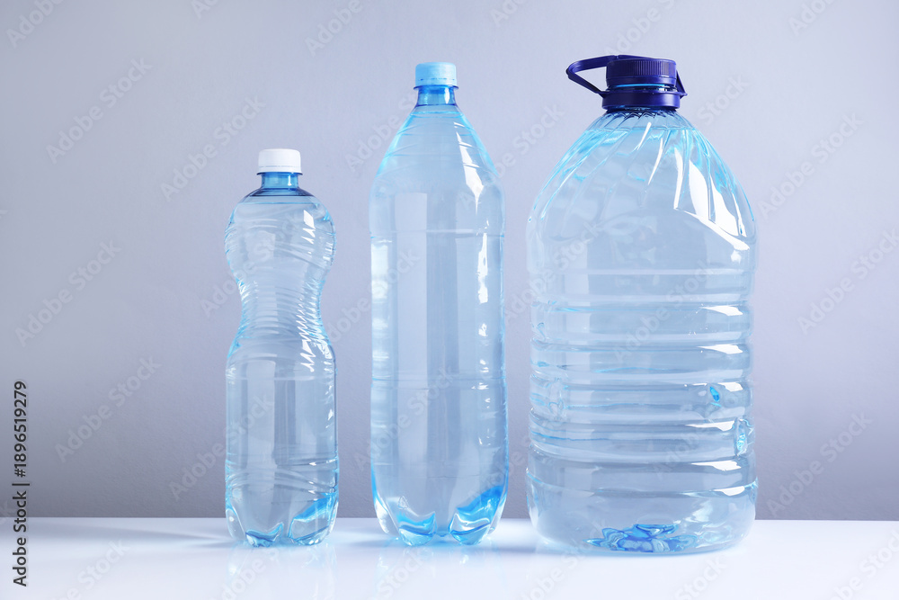 Naklejka premium Water bottles of different sizes on white table against grey background