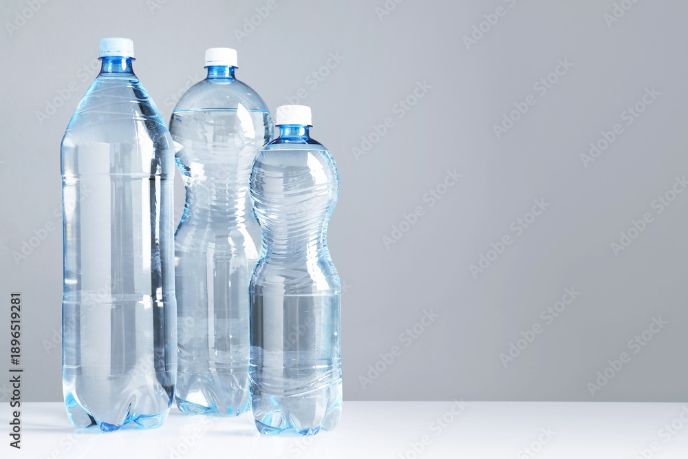 Fototapeta premium Water bottles of different sizes on white table against grey background, space for text