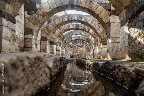 Canvas Print Low angle view of ancient Roman arches reflected in a water canal within the Agora of Smyrna, Izmir, Turkey
