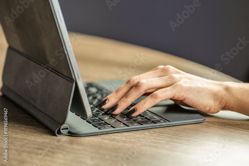 Woman hands typing on tablet keyboard at desk closeup.