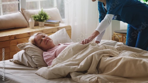 Caregiver covering senior woman patient with a blanket, assisted living care