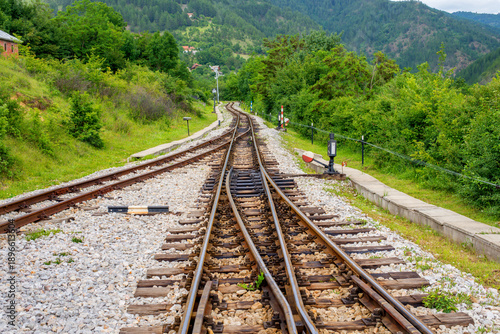 Railway tracks leading through green countryside landscape, representing transportation infrastructure, travel direction, railway logistics, and connection between rural areas.