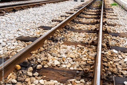 Close up view of railway tracks with gravel and wooden sleepers, showing transportation infrastructure, rail construction details, and industrial background.