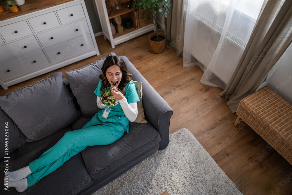 Obraz premium Healthcare worker eating healthy salad on sofa during break