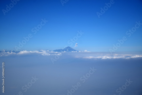 A mountaintop scene with white clouds enveloping it against a backdrop of a clear blue sky