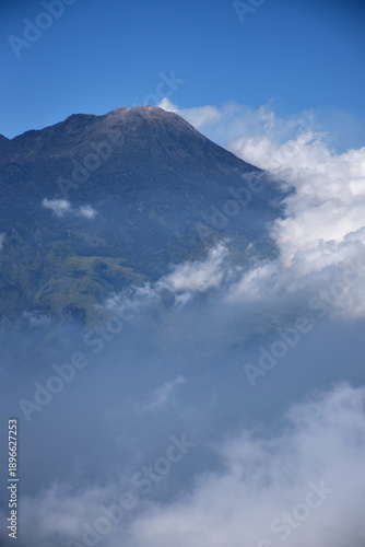 A mountaintop scene with white clouds enveloping it against a backdrop of a clear blue sky
