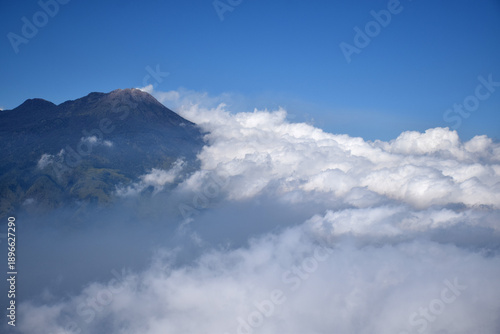 A mountaintop scene with white clouds enveloping it against a backdrop of a clear blue sky