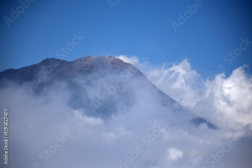 A mountaintop scene with white clouds enveloping it against a backdrop of a clear blue sky